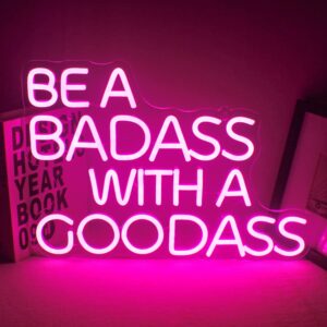 Neon sign reading "Be a badass with a goodass" in bold, glowing letters, mounted on a clear acrylic backboard, perfect for modern or edgy room decor.
