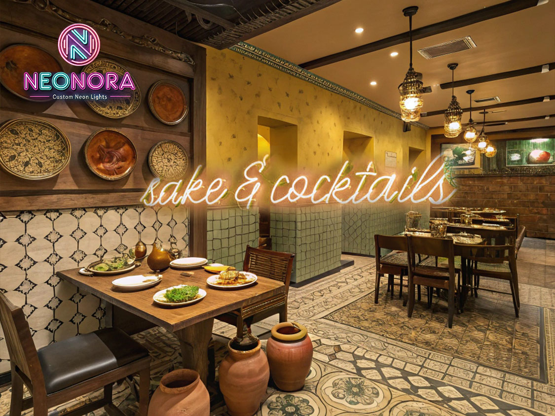 Sake and Cocktails neon sign glowing in indigo blue and magenta LED lights, mounted on a dark brick bar wall.