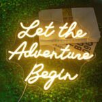 Let the Adventure Begin Neon Sign in warm white, featuring dimmable LED lights. Fun and stylish wall decor for bedrooms, home bars, clubs, weddings, engagement parties, birthdays, and celebrations. USB powered with acrylic backing for easy installation.
