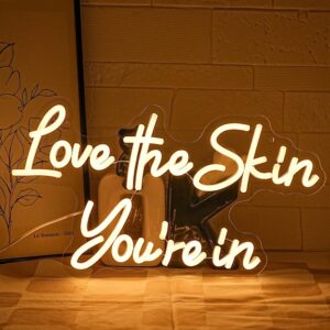 "Love the Skin You're In" warm white neon sign on clear acrylic—perfect for adding an inspiring glow to salons, spas, or beauty spaces.